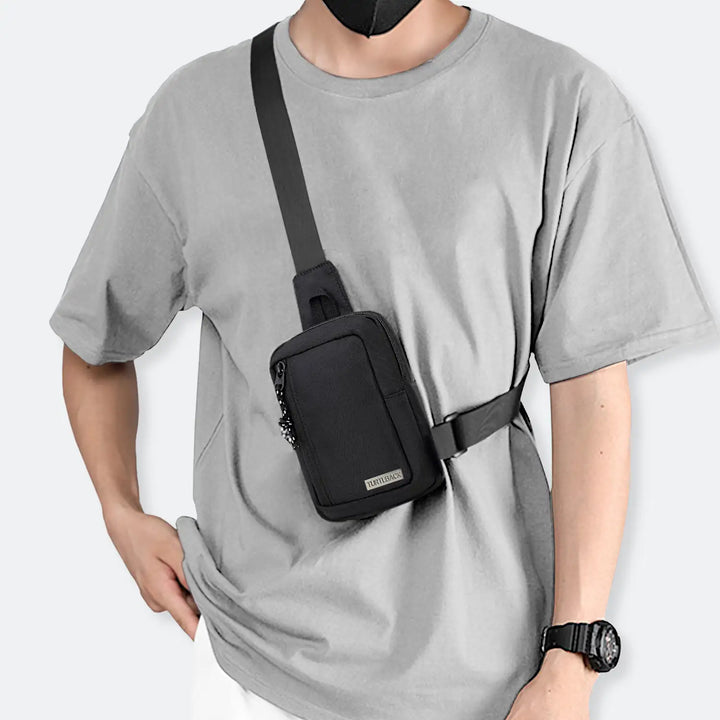 Person mit schwarzer mini Sling Bag grauem T-Shirt und schwarzer Uhr, Mode-Trend 2025