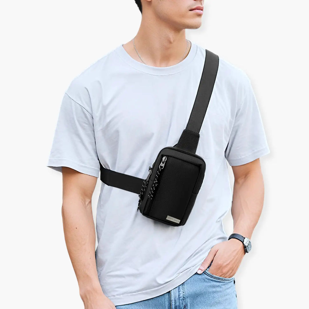 Trendiger junger Mann trägt eine schwarze Sling Bag quer über die Schulter, Mode-Trend 2024