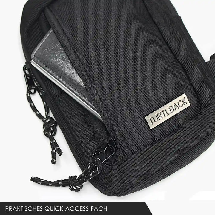 Geöffnete Vorderseite einer schwarzen mini Sling Bag mit Turtlback-Logo und herausragendem Portemonnaie, Kordel-Zipper-Verlängerung